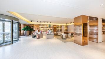A modern hotel lobby with a central reception desk, seating area, and a large potted plant.