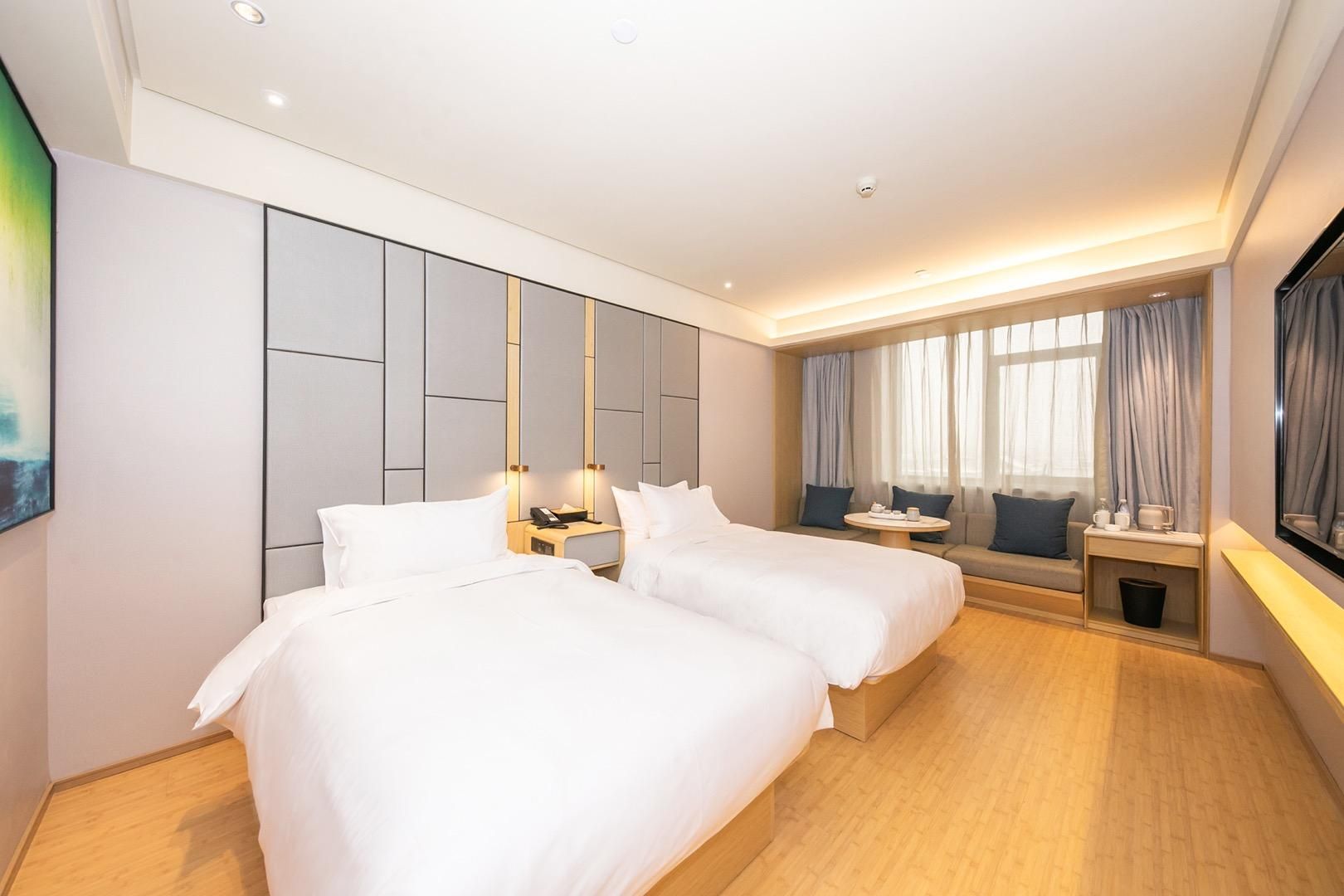 A hotel room with two beds, a seating area with a sofa and a small table, and a large window with curtains.