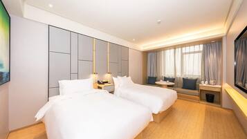 A hotel room with two beds, a seating area with a sofa and a small table, and a large window with curtains.