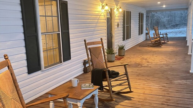 A covered porch with wooden furniture, including chairs and a table, and a view of a snowy landscape. - Charming FarmHouse with animal meet&greet (Mount Jackson)