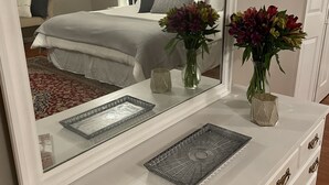 A bedroom with a large mirror, a bed with white bedding, two vases with flowers, and a magazine on the dresser. - Charming FarmHouse with animal meet&greet (Mount Jackson)