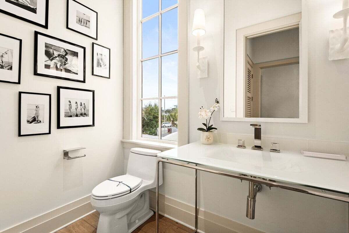 A modern bathroom with a toilet, a glass shower enclosure, a large window, and framed pictures on the wall.