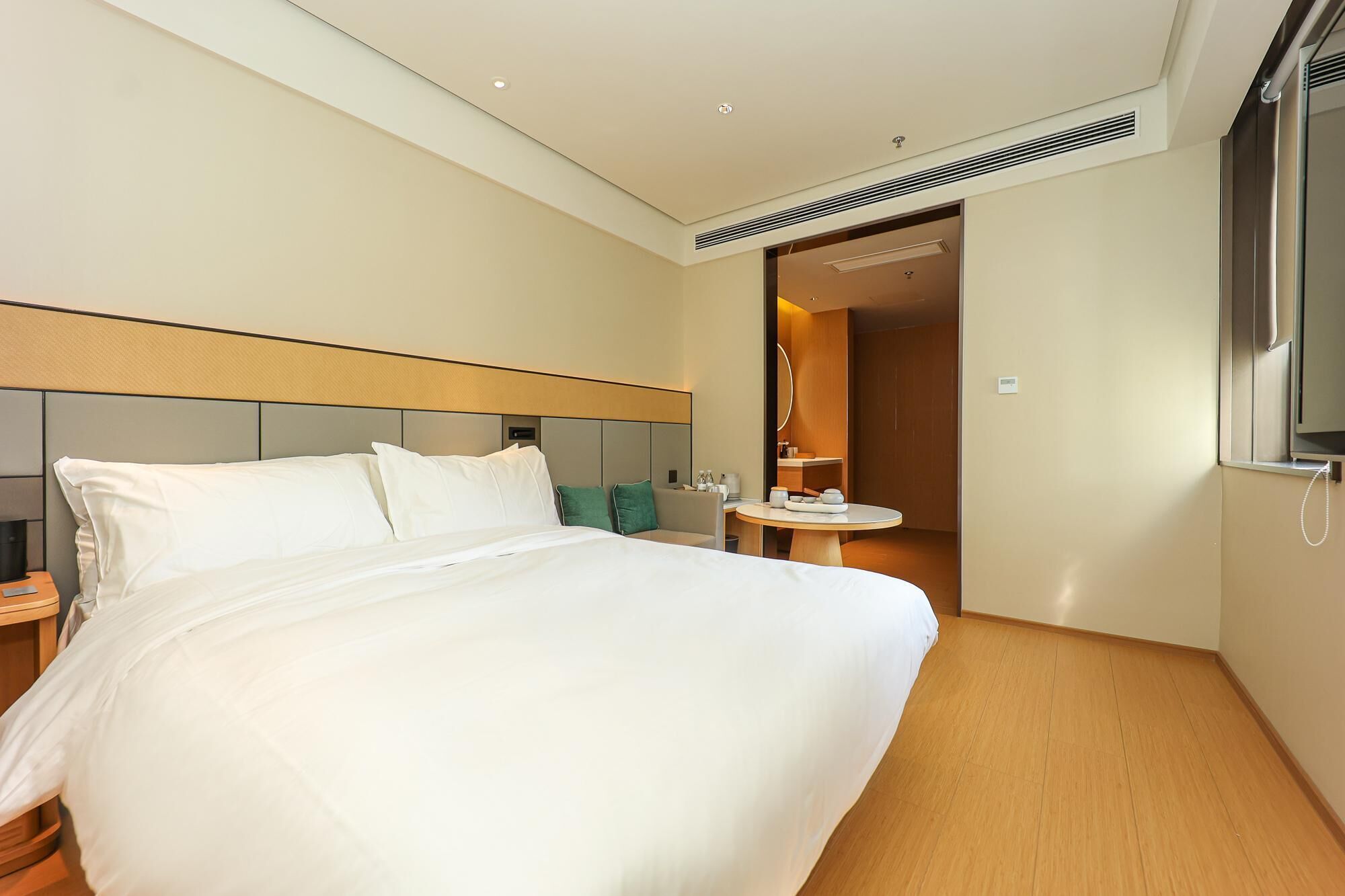 Een hotelkamer met een groot bed, een nachtkastje, een ronde tafel met een stoel, en een badkamer zichtbaar door een open deur.
