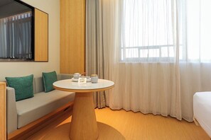 A hotel room with a sofa, a round table with tea set, a bed, and a large window with curtains. - Ji Hotel (Nanchang)