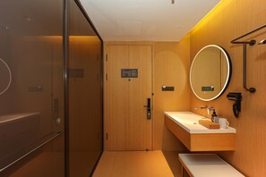A modern bathroom with a wooden vanity, a round mirror, and a glass shower enclosure. - Ji Hotel (Nanchang)