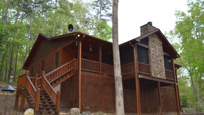 A cabin with a wooden exterior, a stone chimney, and a wooden deck with stairs leading to the main entrance. - Cozy Cabin for 4 with 2 King beds, 2 full baths, 2 fireplaces and upscale Decor! (Morganton)