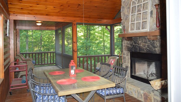 A wooden deck with a stone fireplace, a table with red placemats, and a view of the forest. - Cozy Cabin for 4 with 2 King beds, 2 full baths, 2 fireplaces and upscale Decor! (Morganton)