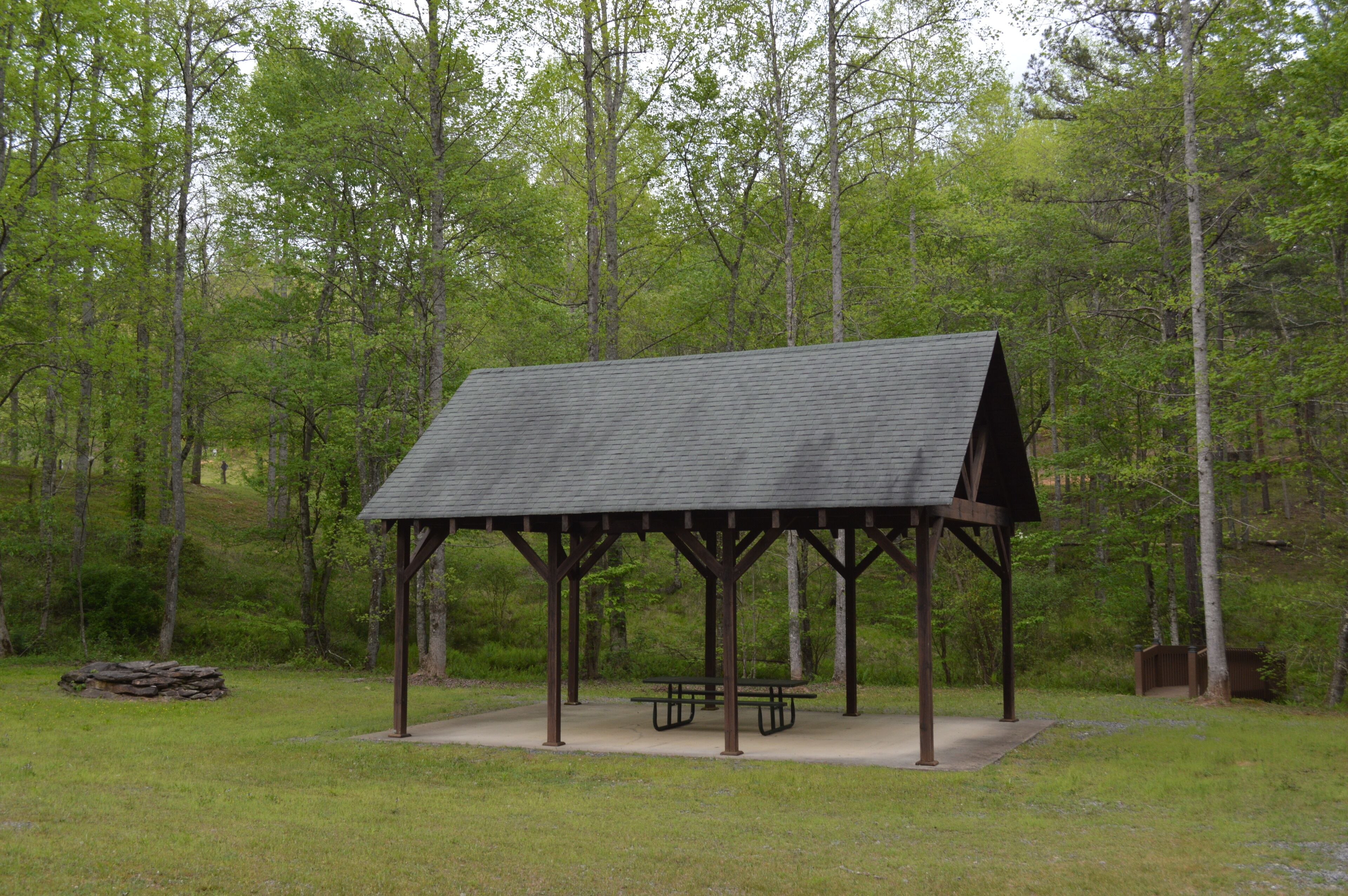 A wooden pavilion with a picnic table in a forested area.