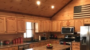 A kitchen with wooden cabinets, a granite countertop, a stainless steel refrigerator, and a large island with bar stools. - Cozy Cabin for 4 with 2 King beds, 2 full baths, 2 fireplaces and upscale Decor! (Morganton)