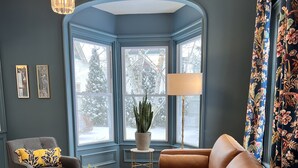 Un salon moderne avec un canapé en cuir marron, un fauteuil gris et une table basse. Une grande fenêtre offre une vue sur les arbres et un paysage enneigé.