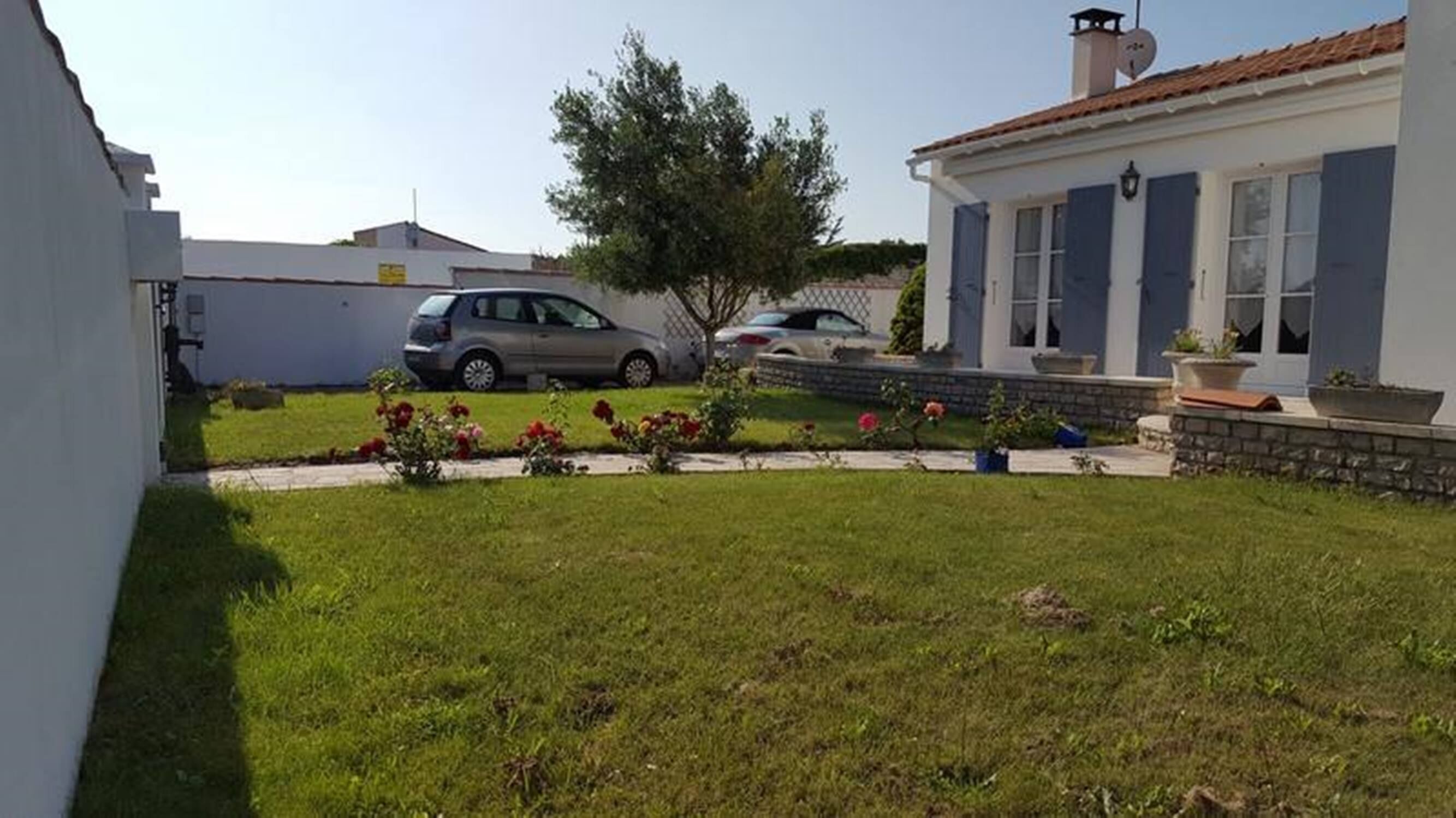 A residential area with a white house, a tree, and two parked cars.