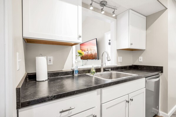 A modern kitchen with white cabinets, a black countertop, a stainless steel sink, and a dishwasher. - Waterview Margaritaville Resort area home. Practice golf! Outdoor TV/grill (Osage Beach)