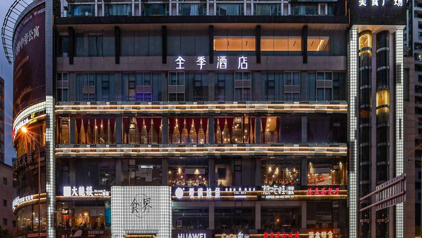 Een hotel met meerdere verdiepingen, een opvallend hotelbord en diverse winkels, waaronder een Huawei winkel.
