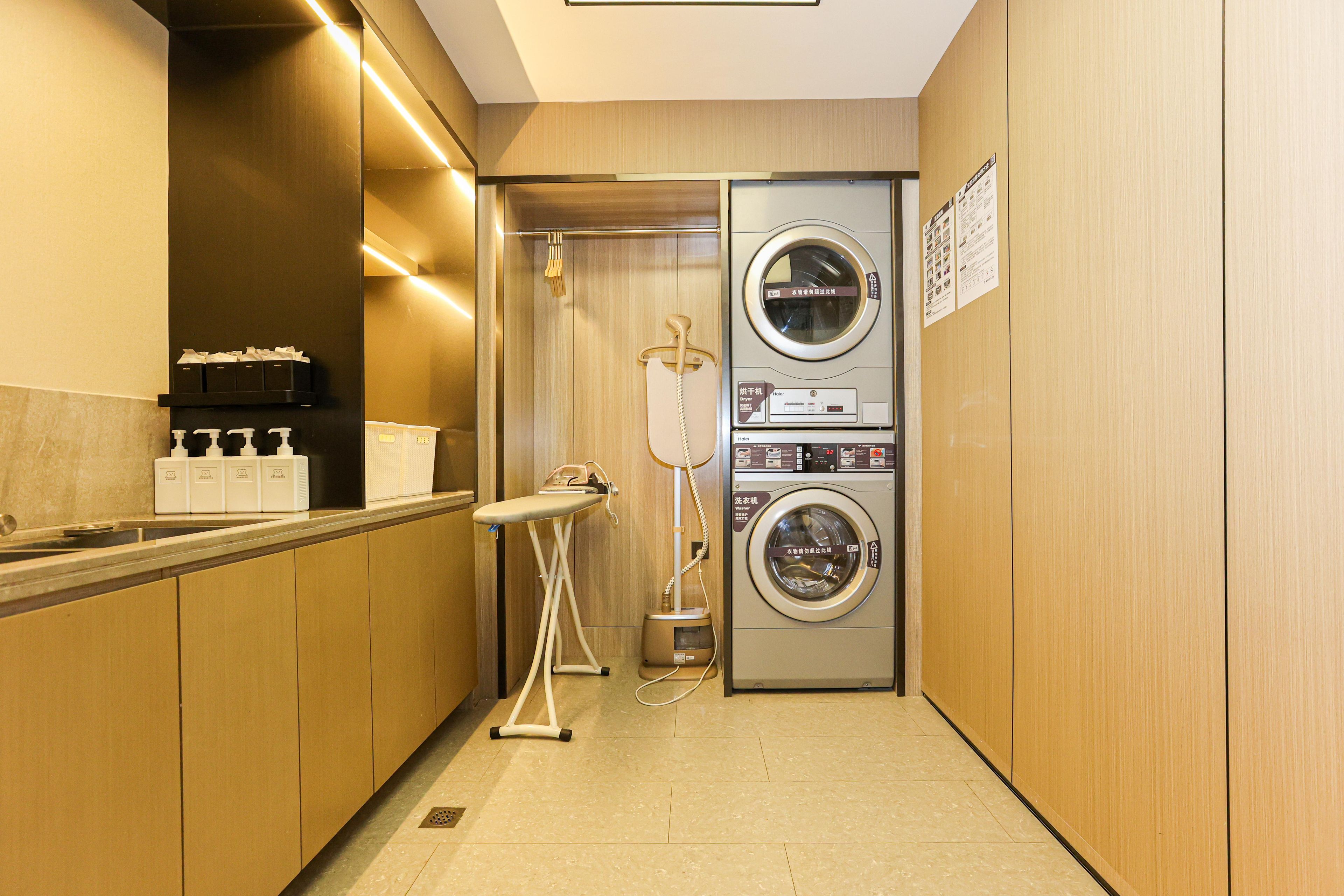 A compact hotel bathroom with a washing machine, dryer, and ironing station.