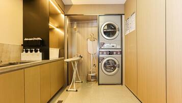 A compact hotel bathroom with a washing machine, dryer, and ironing station.