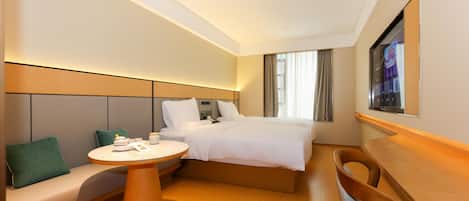 A hotel room with a bed, a sofa, a round table, and a TV mounted on the wall.