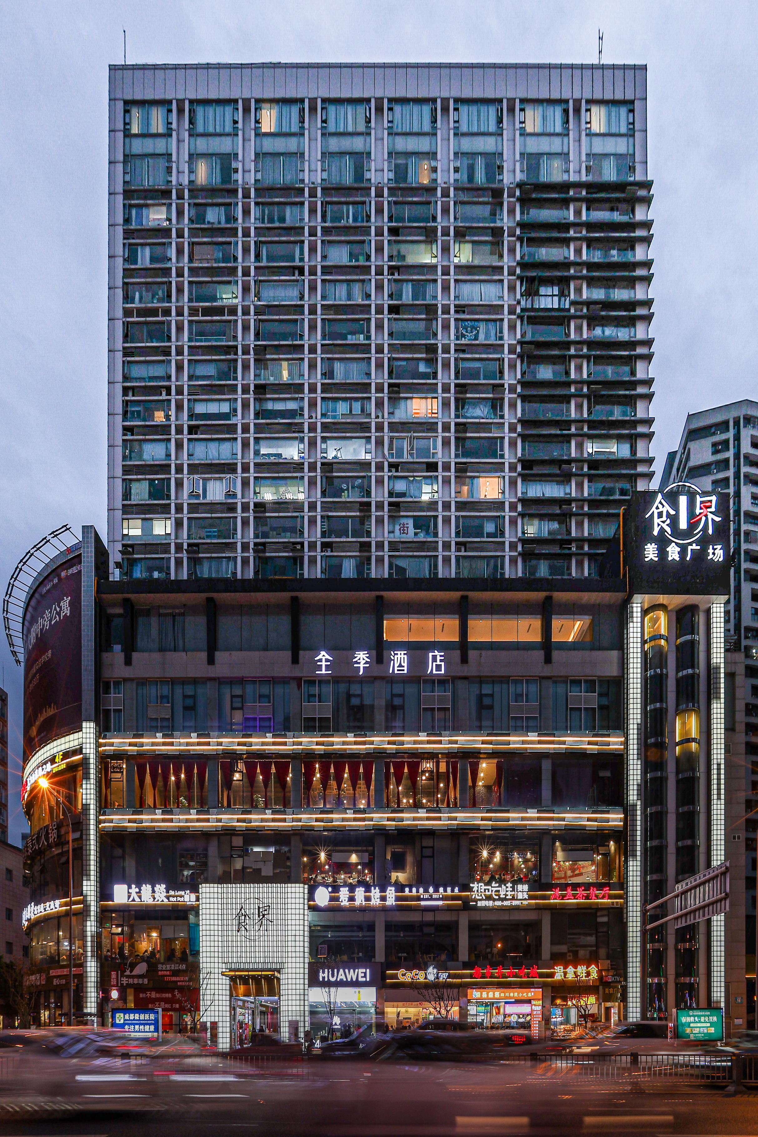 A hotel with multiple floors, a prominent sign for a hotel, and various storefronts including a Huawei store.