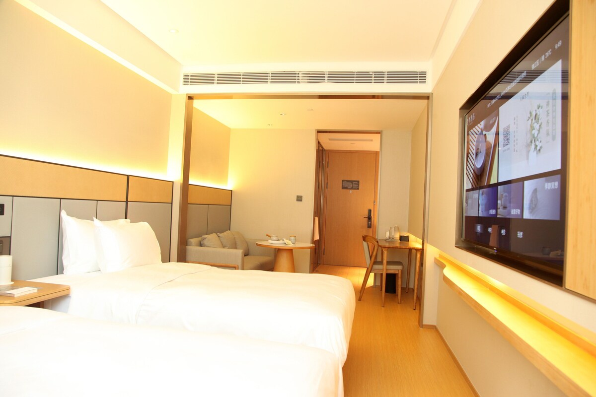 A hotel room with a bed, a sofa, a small table, and a TV mounted on the wall.