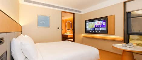 Een hotelkamer met een bed, een bureau met telefoon, een aan de muur bevestigde televisie en een klein tafeltje met een kop en theepot.