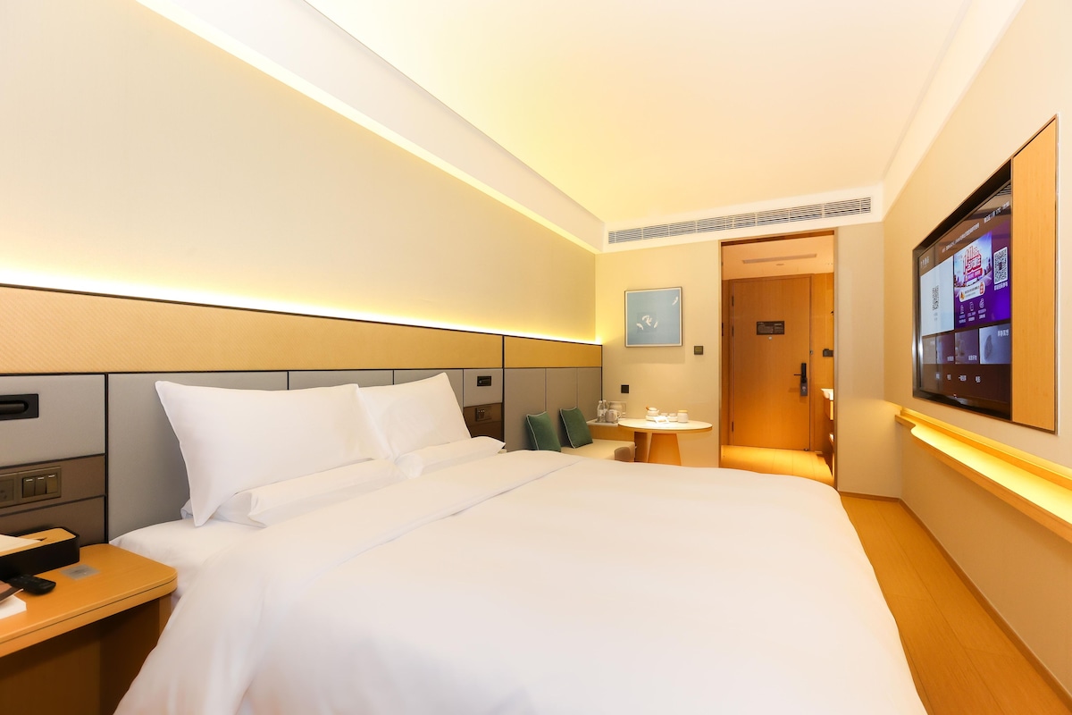 A hotel room with a bed, bedside table, TV, and a small table with a chair.