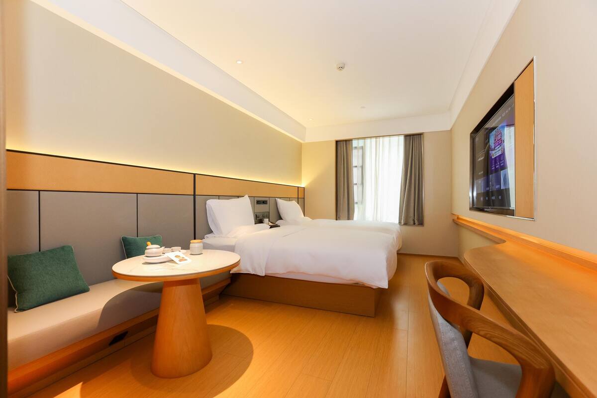 A modern hotel room with a bed, a sofa, a round table, and a TV mounted on the wall.