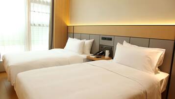 A hotel room with two beds, a bedside table with a phone, and a window with curtains.
