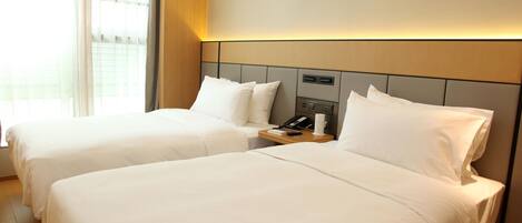 A hotel room with two beds, a bedside table with a phone, and a window with curtains.