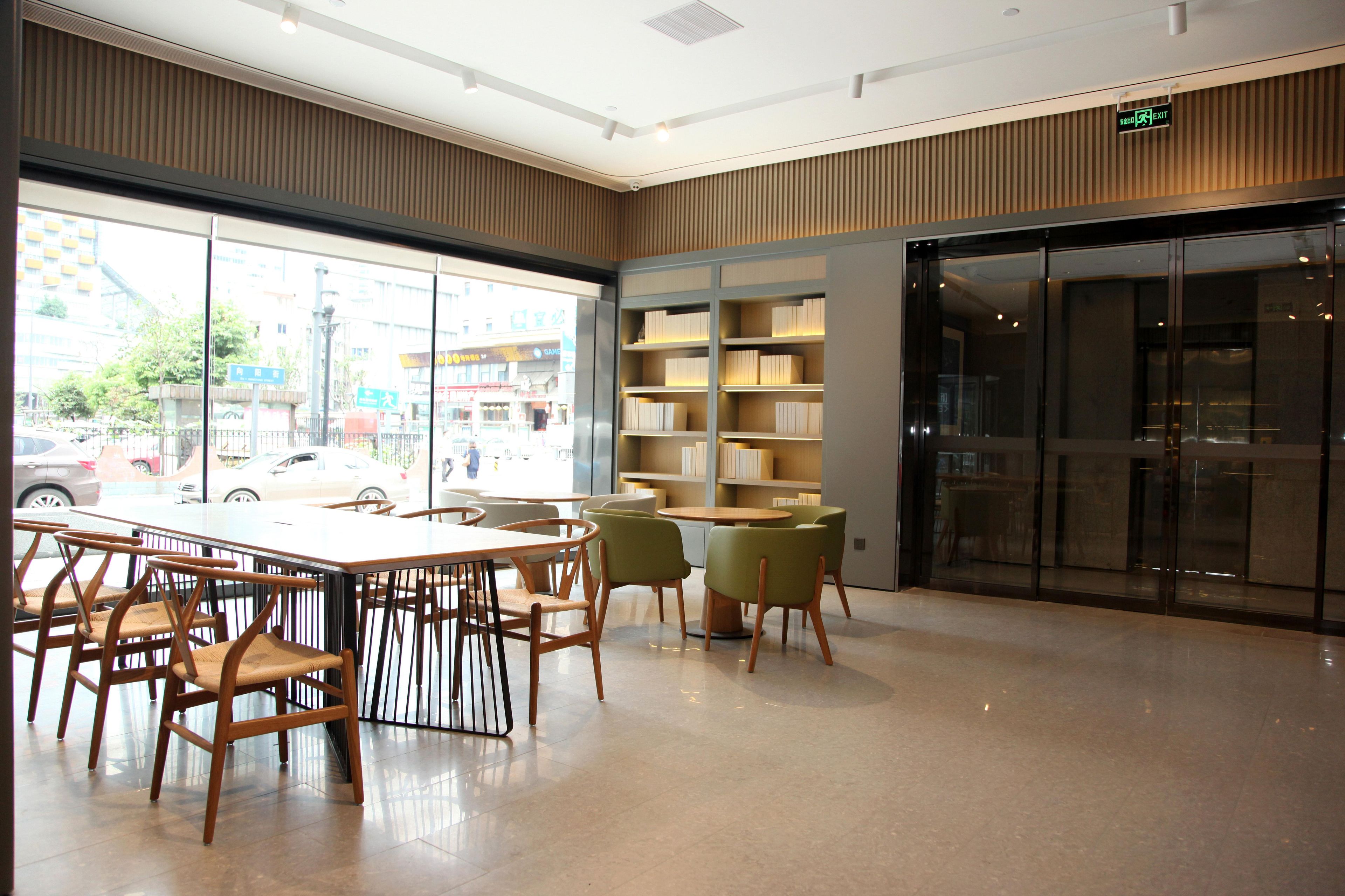 A modern library with a large window, wooden tables, and chairs.