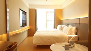 A modern hotel room with a large bed, bedside table, and a view of the city.