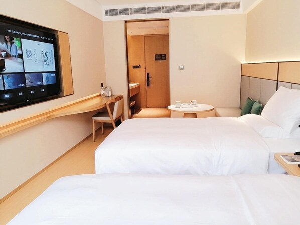 A hotel room with two beds, a desk, a TV, and a small table.