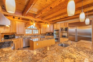 Una cocina amplia con gabinetes de madera, encimeras de granito, electrodomésticos de acero inoxidable e iluminaci ón colgante.