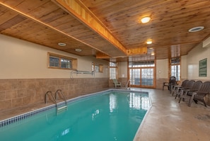 An indoor swimming pool with wooden ceiling beams, tiled walls, and a seating area with chairs.