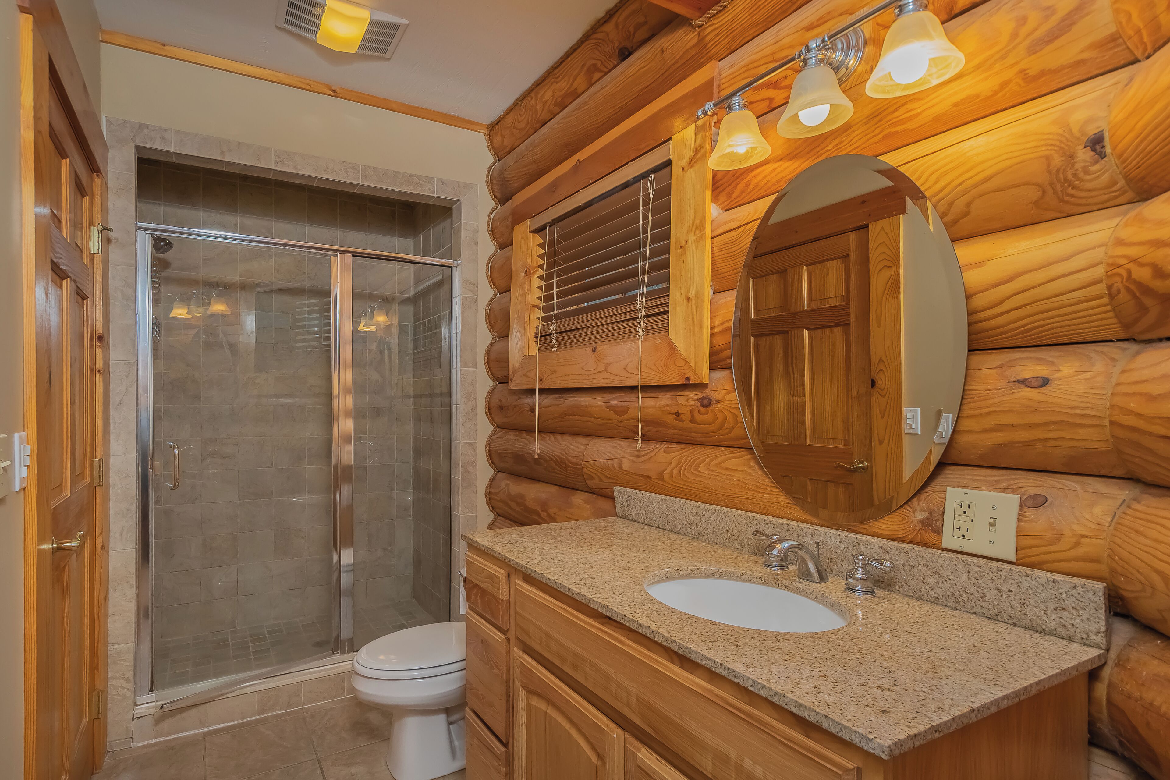 Ein Badezimmer einer Holzhütte mit einer Duschkabine aus Glas, einem weißen Waschbecken und einem Holzbadezimmermöbel.