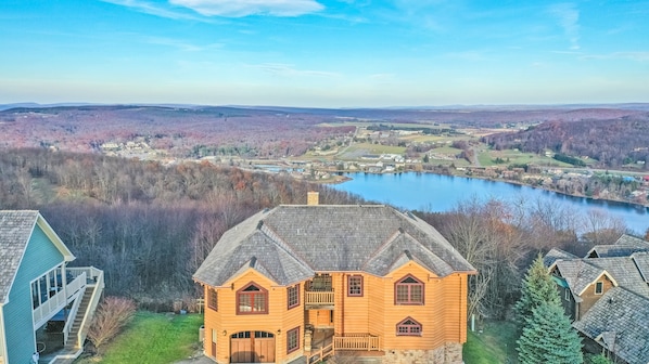 A log cabin with a stone foundation, a front porch, and a view of a lake and surrounding landscape.