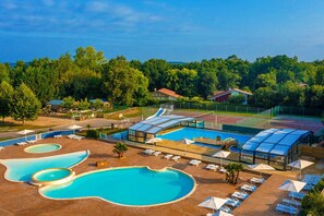 Un resort con varias piscinas, tumbonas y una cancha de tenis.