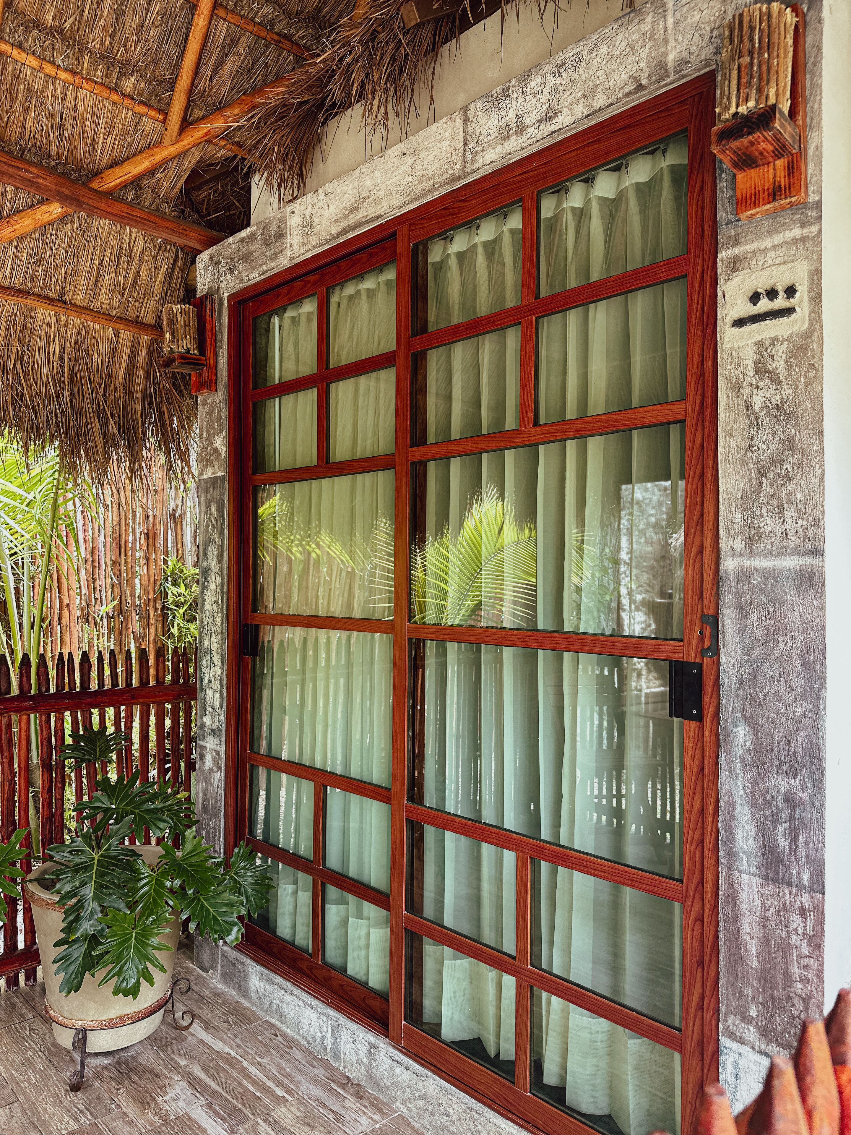 Una habitación con un ventanal grande de madera, techo de paja y una planta en maceta.