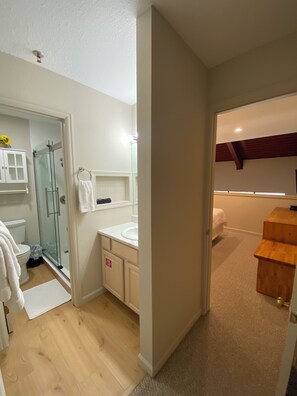 Een moderne badkamer met een glazen douche, witte inrichting en een houten bankje.