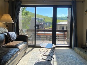 Een kamer met een leren bank, een klein rond tafeltje en uitzicht op een balkon met een leuning.