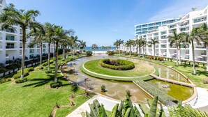 A resort with a central circular water feature, palm trees, and a view of the ocean. - Condo Aria Ocean 306 (Nuevo Nayarit)