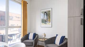 A modern living room with two grey armchairs, a small round table with a globe, and a framed artwork on the wall.