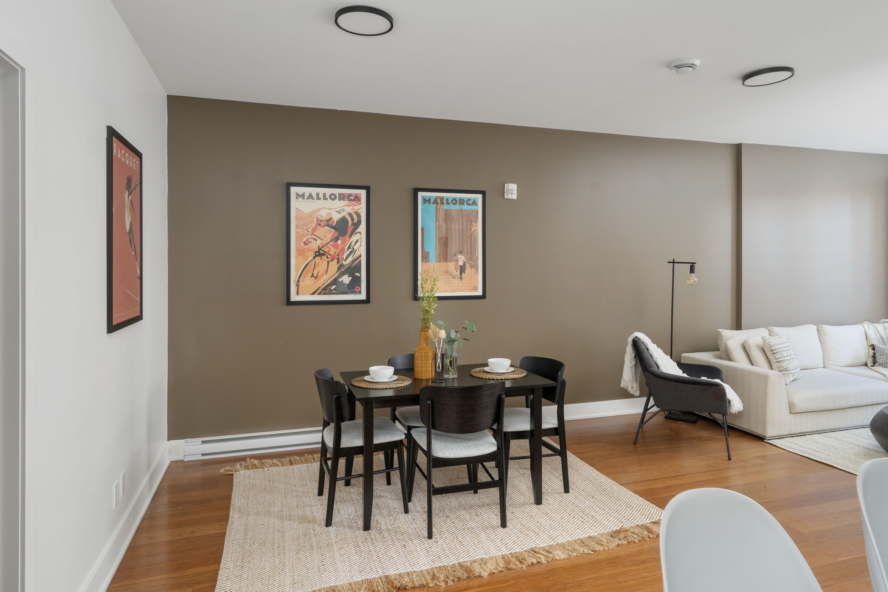 A modern living room with a dining area, featuring a brown accent wall, a white sofa, and a dining table with chairs.