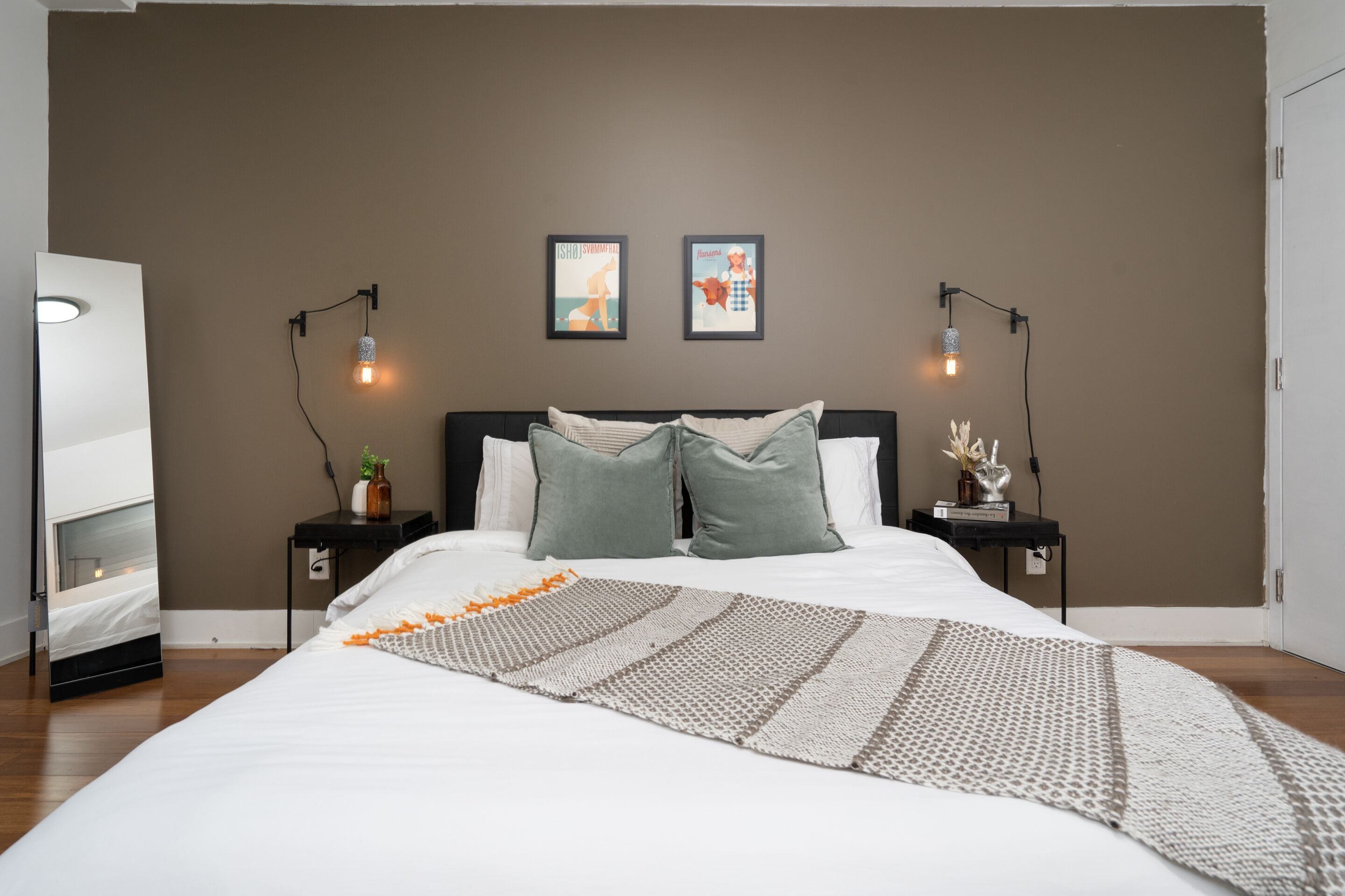 Quarto moderno com uma cama grande, duas mesas de cabeceira e luminárias fixadas na parede.