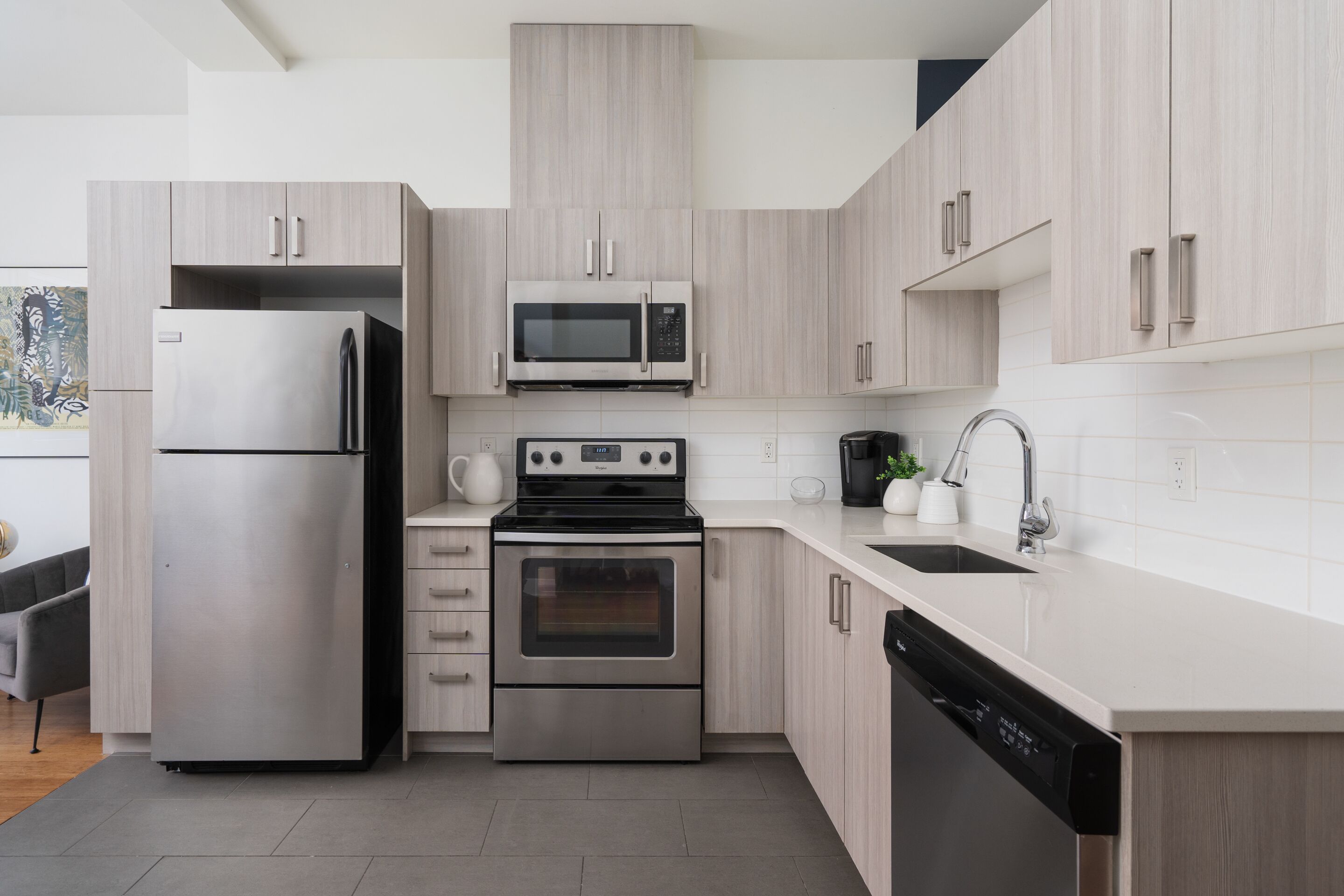 A modern kitchen with stainless steel appliances, light wood cabinets, and a white countertop.
