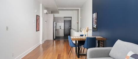 Una sala de estar moderna con un sofá gris, una mesa de comedor con sillas azules y una cocina al fondo.