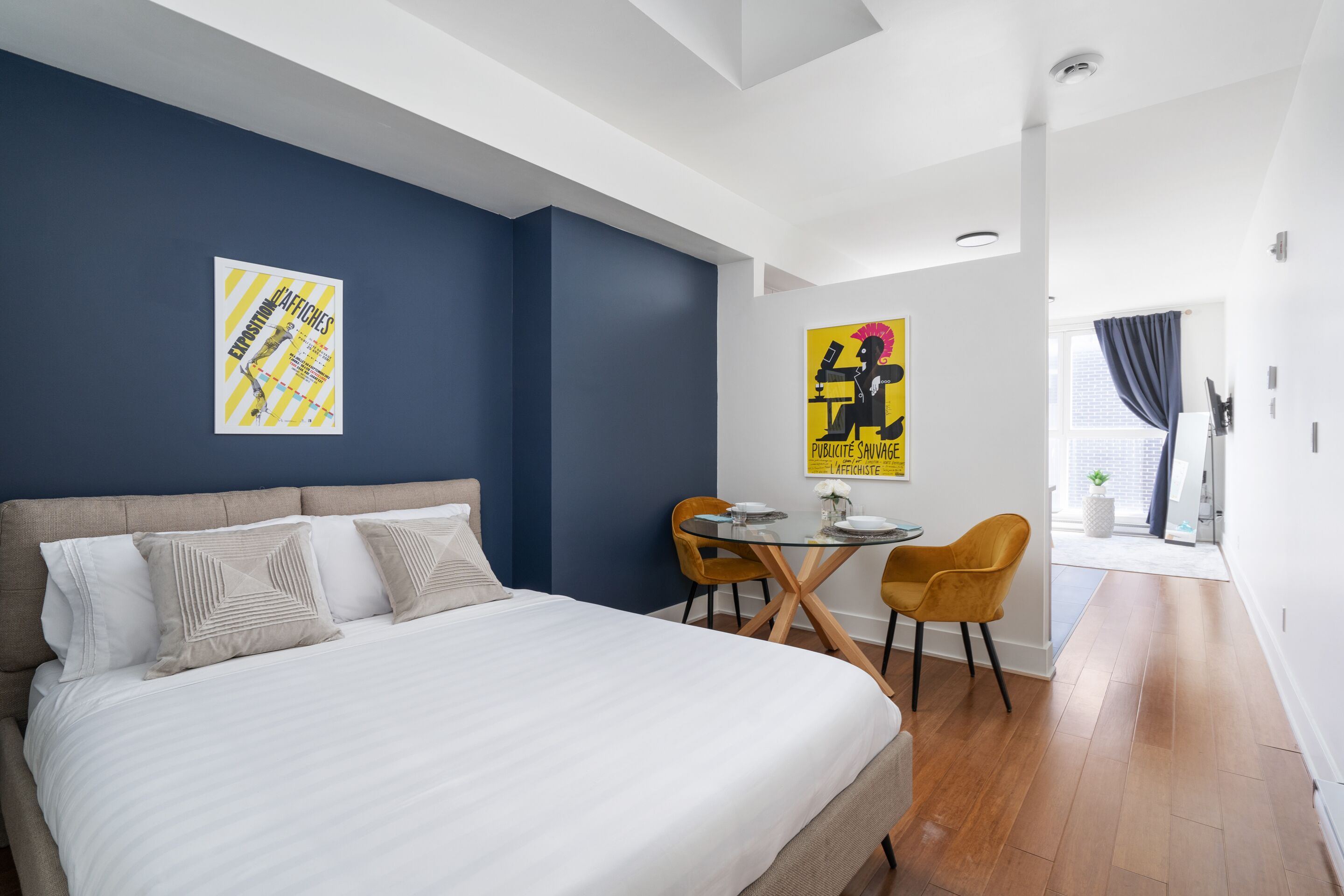 Una habitación de hotel moderna con una cama grande, una mesa de comedor con sillas y obras de arte en las paredes.