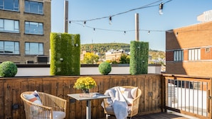 Un patio en la azotea con sillas de mimbre, una mesa pequeña y una planta en maceta.