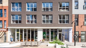 Un edificio moderno con fachada de ladrillo, amplias ventanas y una entrada acogedora con un banco y plantas en macetas.