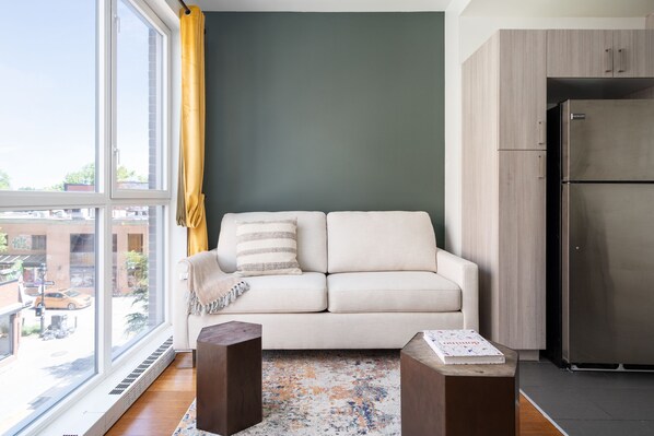 A modern living room with a sofa, a coffee table, and a large window with a view of the outside. - ApartHotel Prince Arthur (Montreal)