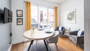 Una sala de estar moderna con una mesa de comedor redonda, un sofá gris y un televisor montado en la pared.