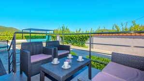 Eine Terrasse mit Korbmöbeln, einem Pool und Blick auf Grünflächen und Hügel.